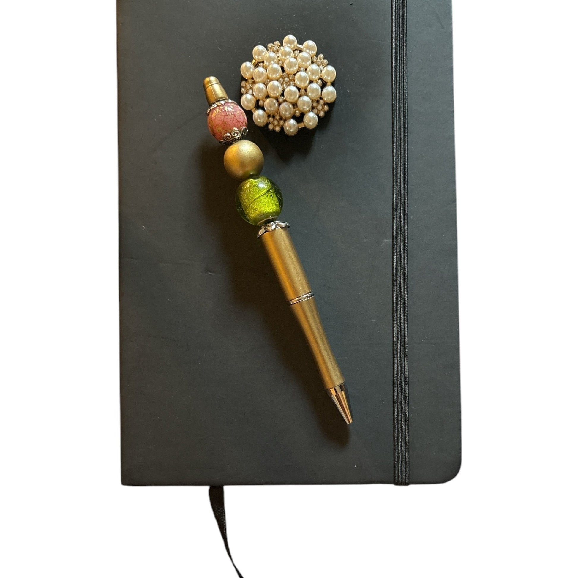 House of Lux Gifts beaded pen with pink, gold, and green beads on a black journal with a pearl brooch accessory.