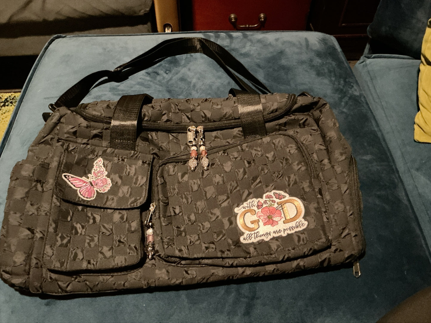 House of Lux Gifts black textured checkered duffel bag with floral butterfly patches and beaded zipper pulls