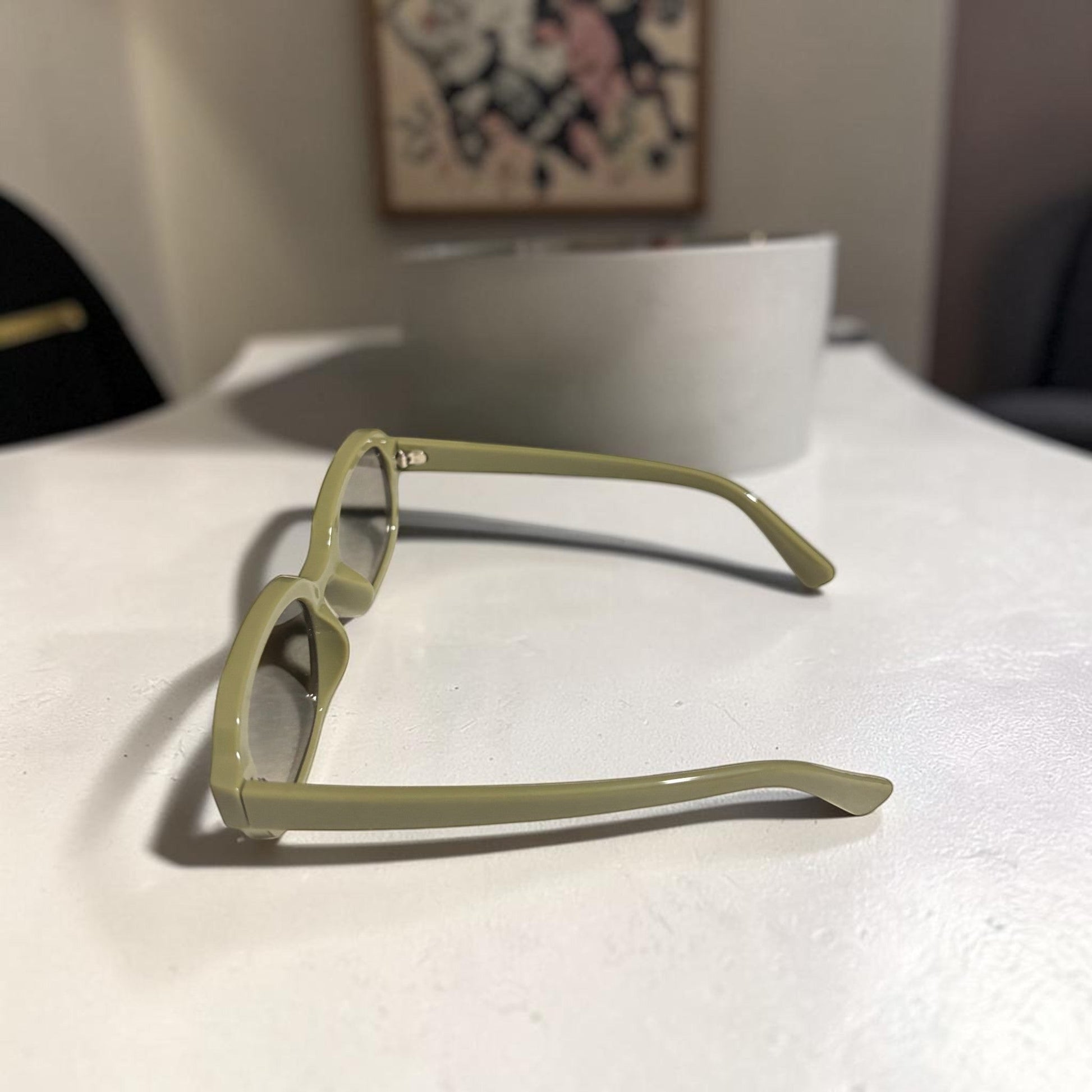 House of Lux Gifts olive green sunglasses with a sleek rectangular frame resting on a white surface