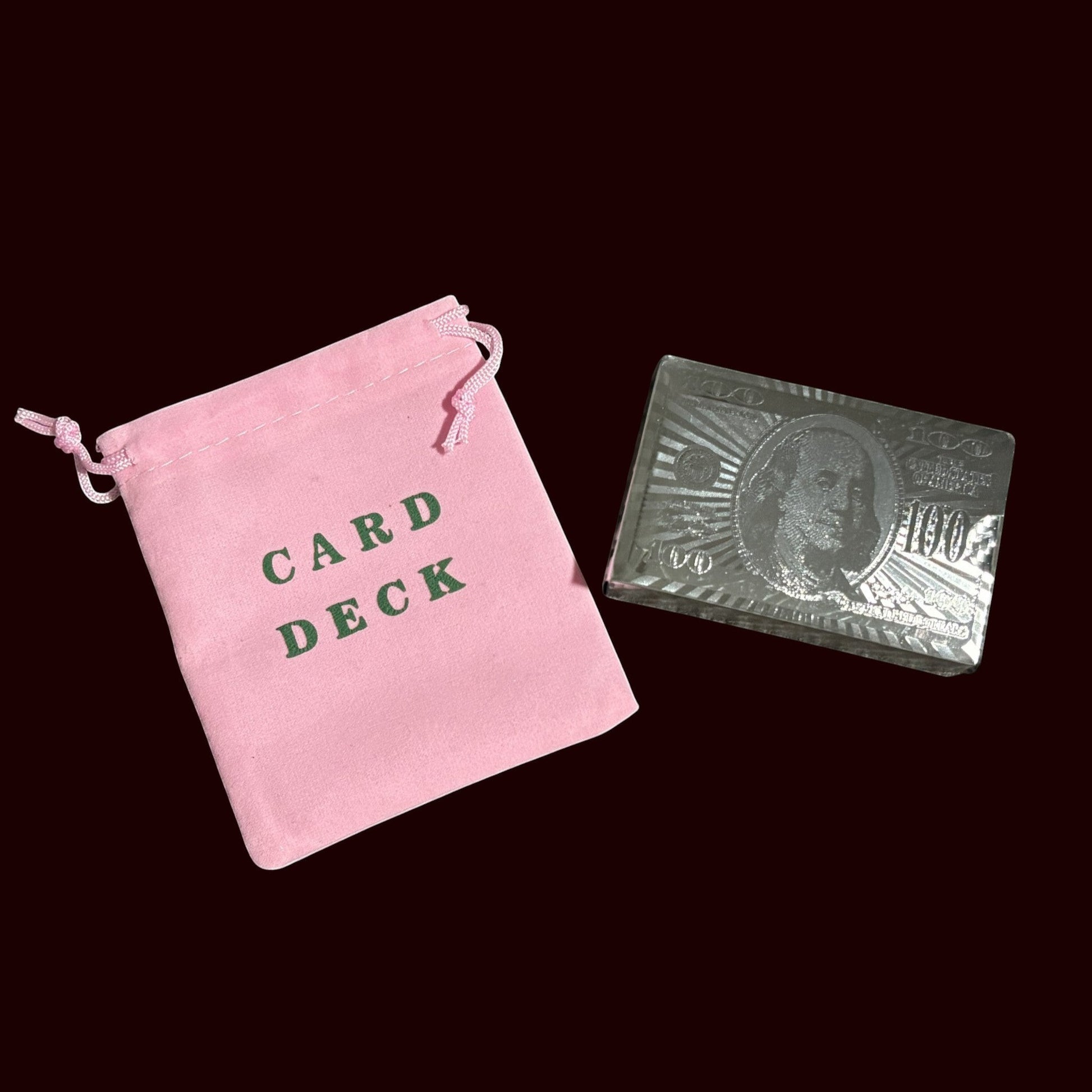 House of Lux Gifts pink velvet drawstring bag labeled Card Deck next to a silver hundred dollar bill playing card deck